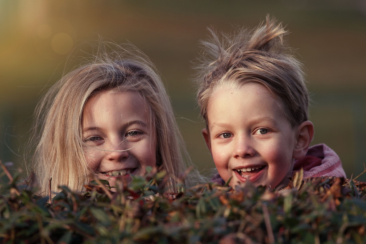 Zwei Kinder schauen mit zerzausten Haaren lächelnd in die Kamera